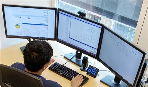 Utvikler hos DOPS foran tre skjermer med kode og dashbord